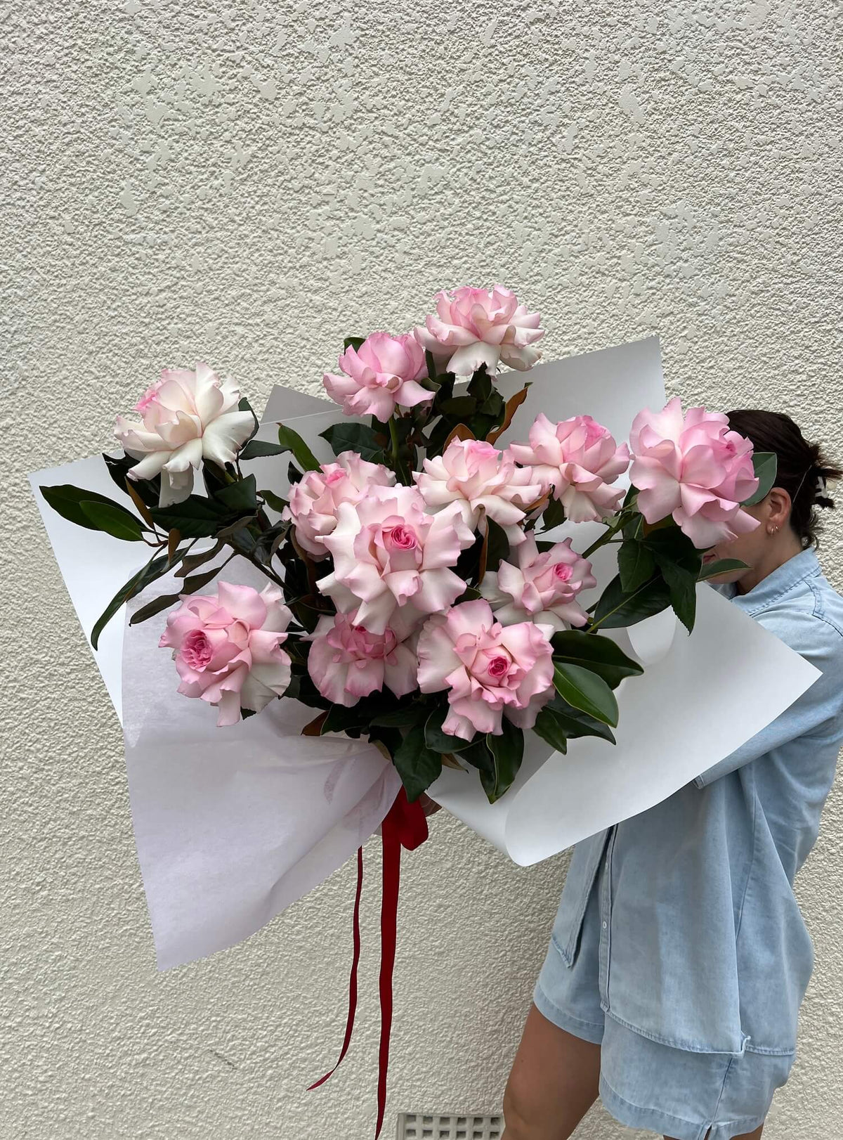 Person holding a bouquet of big pink roses for Valentines against a plain wall
