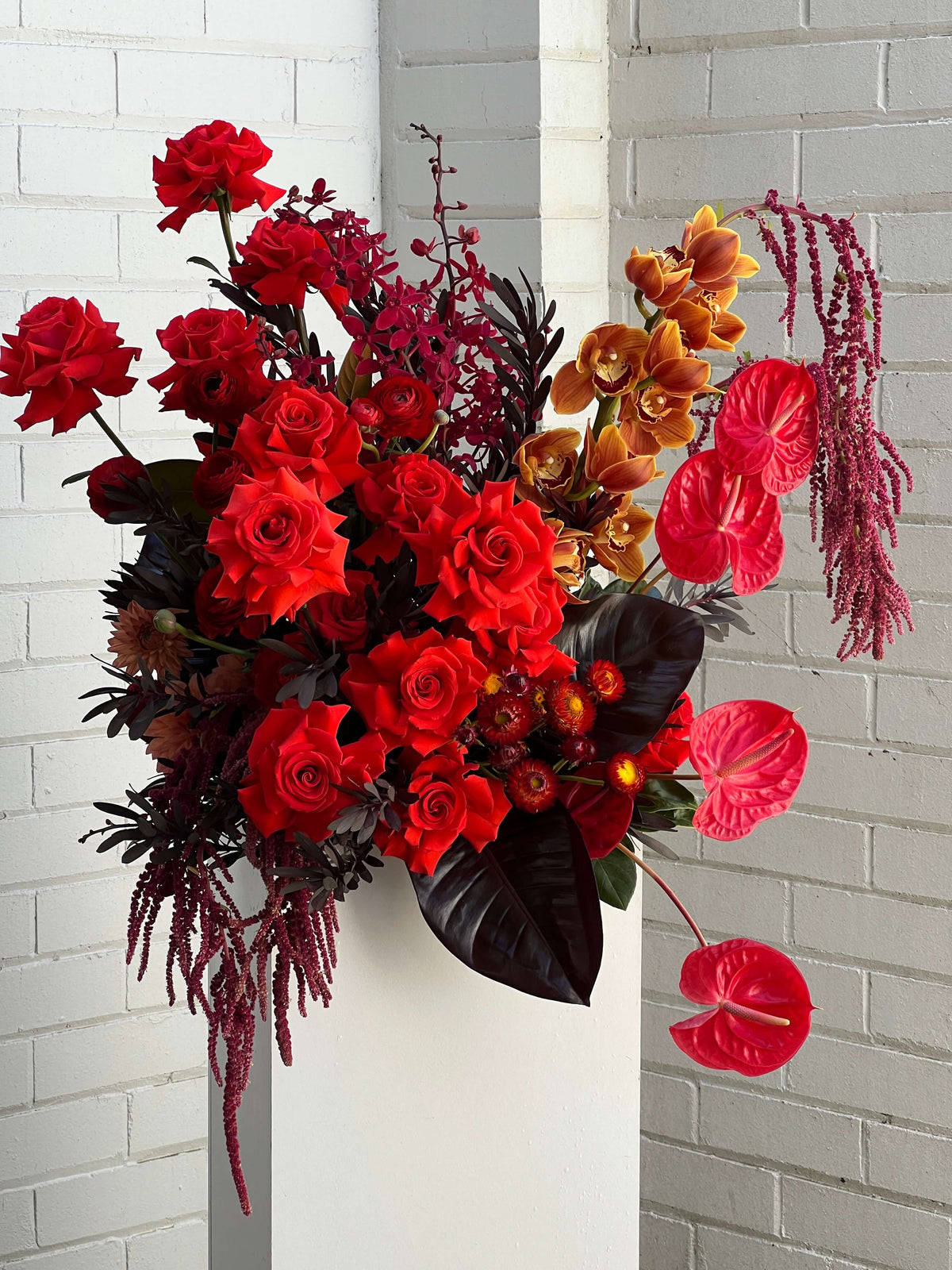 Bouquet of red roses and orange orchid flowers against a white brick wall